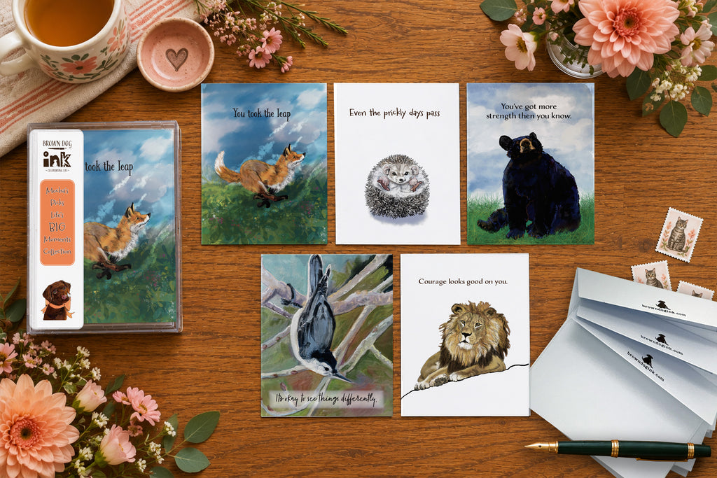 Life’s Big Moments greeting card collection featuring five illustrated encouragement and milestone cards with original artwork by Susan J. York, displayed with Brown Dog Ink packaging and envelopes on a warm floral tabletop.