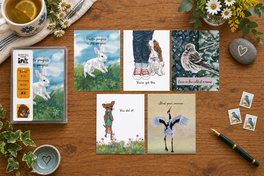 Encouraging Words #2 greeting card collection featuring five illustrated animal encouragement cards with a rabbit, beagle, redpoll, Chihuahua and snow crane, with original artwork by Susan J. York, displayed with Brown Dog Ink packaging on a warm tabletop.