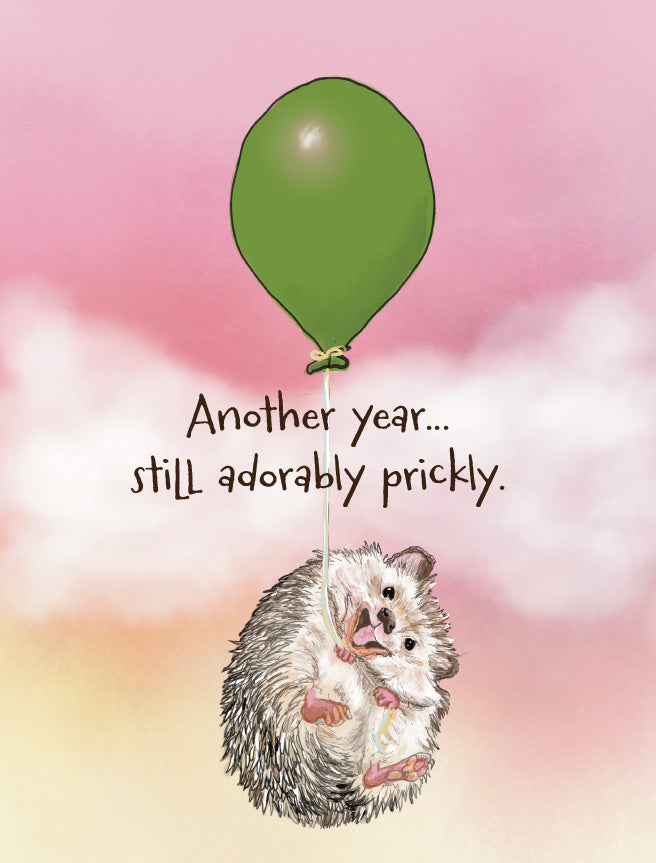 A cute illustration of a small hedgehog clinging to the string of a green balloon against a pink sky with clouds. The text reads, 'Another year. Original artwork by Susan J. York.