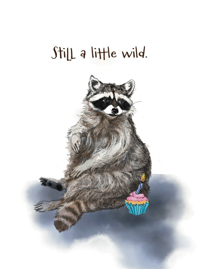 A whimsical illustration of a raccoon sitting upright on a white background, with the text 'Still a little wild.' above it and a small pink cupcake with a blue wrapper and candle beside it. Original artwork by Susan J. York.