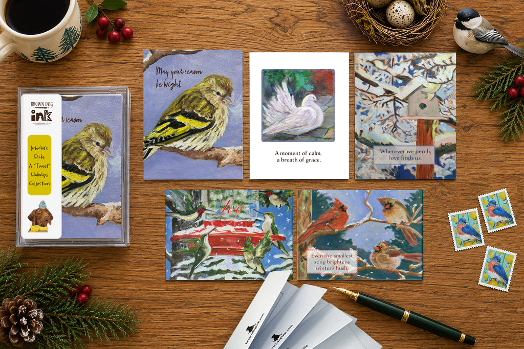 Five illustrated bird holiday cards from Brown Dog Ink’s A “Tweet” Holidays Collection, featuring original artwork by Susan J. York, displayed with the boxed card set on a festive winter tabletop.