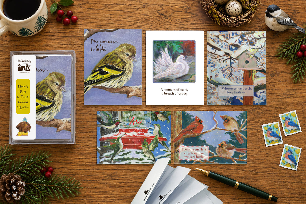 Five illustrated bird holiday cards from Brown Dog Ink’s A “Tweet” Holidays Collection, featuring original artwork by Susan J. York, displayed with the boxed card set on a festive winter tabletop.