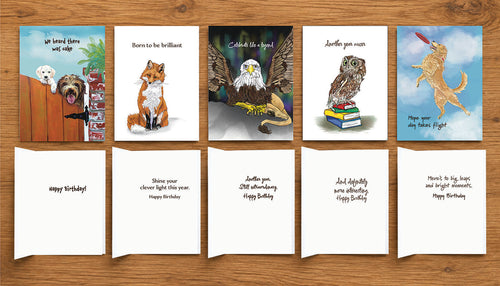 Five illustrated animal birthday cards by Susan J. York arranged on a wooden surface, showing the colorful front artwork and coordinating inside birthday messages.